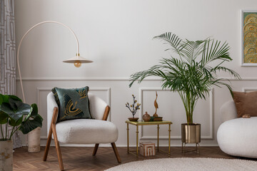 Warm composition of living room interior with boucle armchair, sofa, plant in gold pot, green pillows, round rug, stylish coffee table, wall with stucco and personal accessories. Home decor. Template.