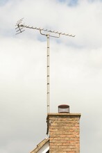 Weathered Chimney Pot On Red Brick Stack With TV Aerial Against Cloudy Sky