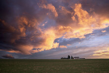 Sunset View On A Green Field With Purple And Blue Clouds And A Farm Silhouette Against