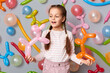 © sementsova321 - Funny birthday kid. Playing time. little girl with braids standing against gray wall decorated with colorful balloons, smiling happy enjoying holiday.