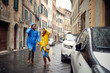 © luckybusiness - A young cheerful couple in raincoats is running away from the rain while walking the city. Walk, rain, city, relationship