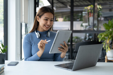 Attractive young Asian woman using tablet while sitting at her desk in the living room.