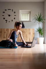 Young woman in casual clothing sitting on a mat in domestic living room using a laptop computer