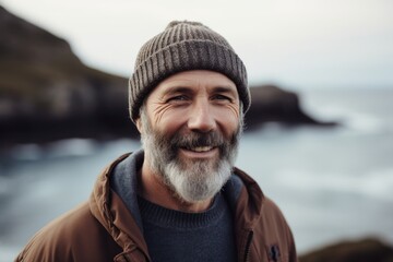 Wall Mural - Portrait of a smiling senior man standing by the sea wearing a hat