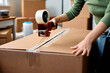Close up of woman using tape dispenser while packing boxes before moving out of her apartment.