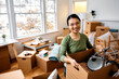 © Drazen - Happy Asian woman carrying her belongings into new home and looking at camera.