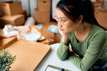 Wall Mural - Pensive Asian woman among her belongings in new apartment.