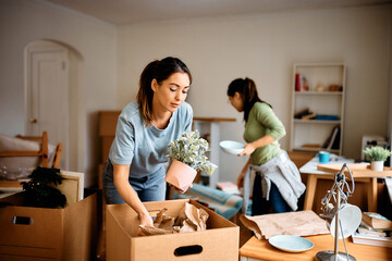 Wall Mural - Young woman and her friend packing their belongings while preparing to move out of apartment.