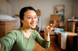 © Drazen - Happy Asian woman takes selfie while holding key of her new home and looking at camera.
