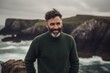 © Robert MEYNER - Portrait of a smiling bearded man in a green sweater standing on a cliff by the sea