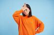 Epic fail. Disappointed asian woman slaps her forehead with upset face, forgot smth, annoyed, stands over blue background in orange sweatshirt
