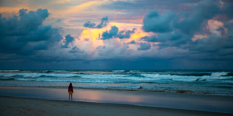 Wall Mural - Beautiful girl in pink blouse walks on stunning vast Patchs beach near Byron Bay and admires colorful cloudy sunset. New South Wales, Australia.