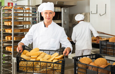 Wall Mural - Positive man worker of bakery carrying box of bread standing at kitchen