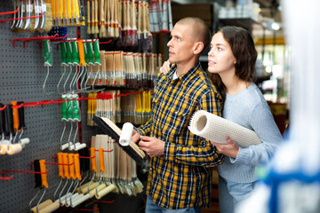 Wall Mural - Smiling couple, woman and man, standing with goods in hands in hardware store