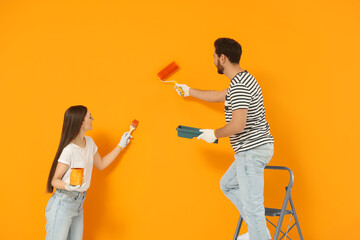 Poster - Designers painting orange wall with roller and brush