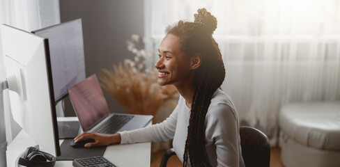 Wall Mural - smiled cheerful female web expert sitting at desk in living room coding on computer
