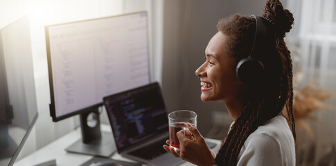 Wall Mural - side view of cheerful young female wearing headphones and programming on computer