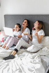 Wall Mural - latin women family mother and daughters enjoying live stream or watching a movie with laptop on bed together in Latin America, hispanic female family