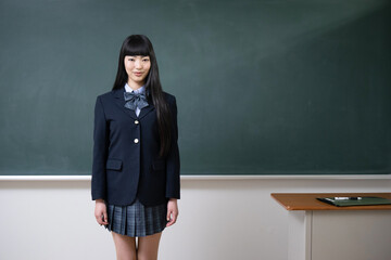 Wall Mural - Asian high school girl looking at the camera in front of the blackboard in a school classroom