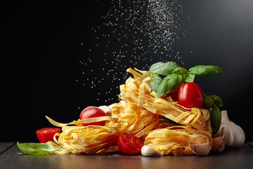 Homemade raw pasta with tomato, garlic, and basil on a black background.