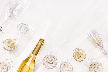 Wall Mural - Top view white sparkling wine bottle, set colored glasses wine with sunshine shadow and flare on light white background. White wine aesthetic flat lay, copyspace. Summer still life light alcohol