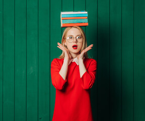 Wall Mural - Stylish blond hair woman in red dress with book on head on green wooden background