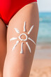 © sosiukin - Woman sunbathing on the beach with a drawing of sun on her leg with sunscreen cream
