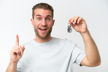 Wall Mural - Young caucasian man holding home keys isolated on white background pointing up a great idea