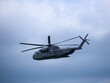 Ein militärischer Hubschrauber mit offener Heckklappe am Himmel.
