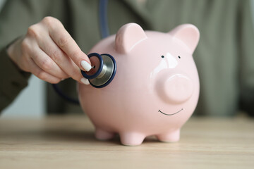 Wall Mural - Woman checks condition of piggy bank with stethoscope