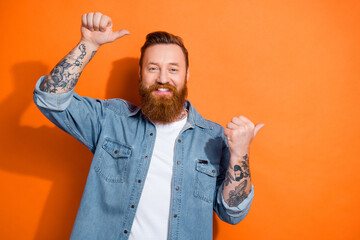 Wall Mural - Photo of satisfied young man stylish wearing jacket direct fingers empty space barbershop beard tattoo salon isolated on orange color background