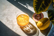 © ADDICTIVE STOCK - Generative AI illustration with high angle of glass of yellow cocktail iced juice with fresh and sliced yellow fruit placed on grey table beside flat leave shades in sunlight outdoors