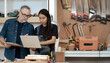 © Nassorn - Multicultural family working at wood craft carpenter's shop as small business owner. American craftsman and Asian wife checking order for handmade furniture DIY. Diversity couple in artisan woodwork.