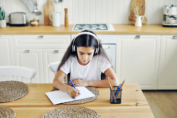pretty pre-teen girl in wireless headphones writing task