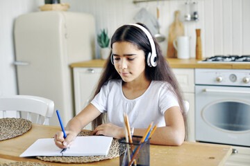 pretty pre-teen girl in wireless headphones writing task
