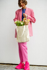 Wall Mural - Stylish woman in pink suit with eco handbag and flowers on white background. Canvas bag with blank space