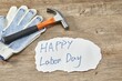 Wide shot of a paper with happy labour day written on it, close to a hand glove and a hammer