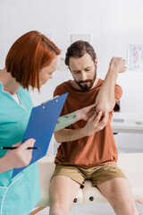 Wall Mural - physiotherapist with digital tablet examining painful elbow of bearded man in hospital.