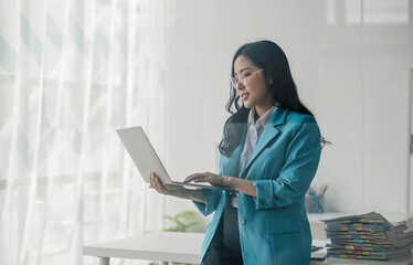 portrait of young asian woman in casual clothes standing holding laptop and looking at camera while 