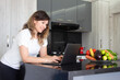 © Henrry L - A beautiful woman smiles as she works on her laptop at a table in her kitchen at home