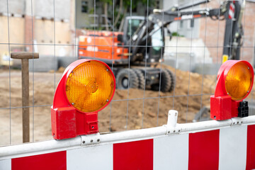 Close-up detail view orange flasher safety blinker light barrier against fence construction site work area. Security equipmnent barricade fuse lamp city street building construction machinery traffic