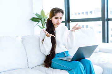 shock content concept with shocked by the news young woman sits on the couch with laptop making hand
