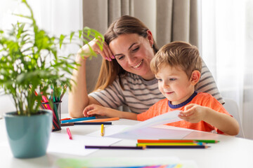 Mother and child drawing with pencils sitting at the desk at home