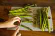 View of slicing fresh asparagus, hands holding knife and cutting clean asparagus.