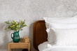 cozy bedroom with white bed linen, pillows and jug with bloom flowers