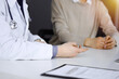 © rogerphoto - Unknown male doctor and patient woman discussing something while sittingin a darkened clinic, glare of light on the background. Close-up of hands