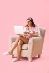 Poster - Young woman using laptop in armchair on pink background