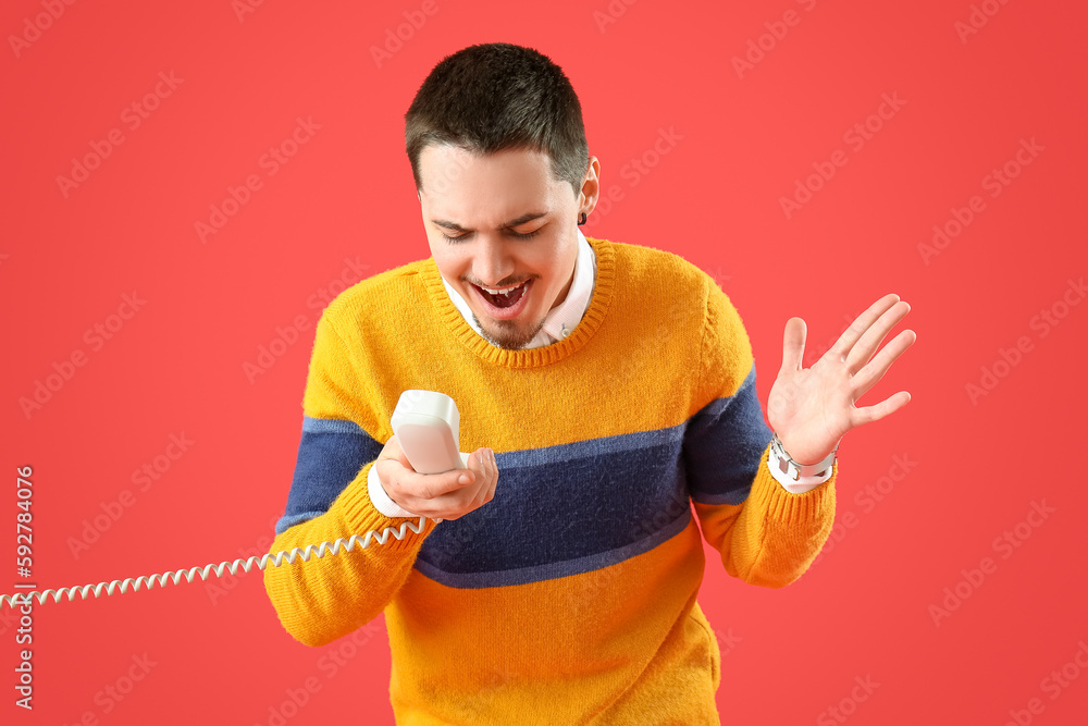 Angry young man with phone receiver on red background