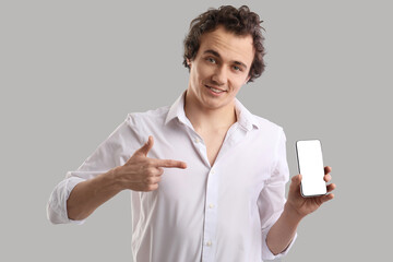 Wall Mural - Young man pointing at mobile phone on grey background