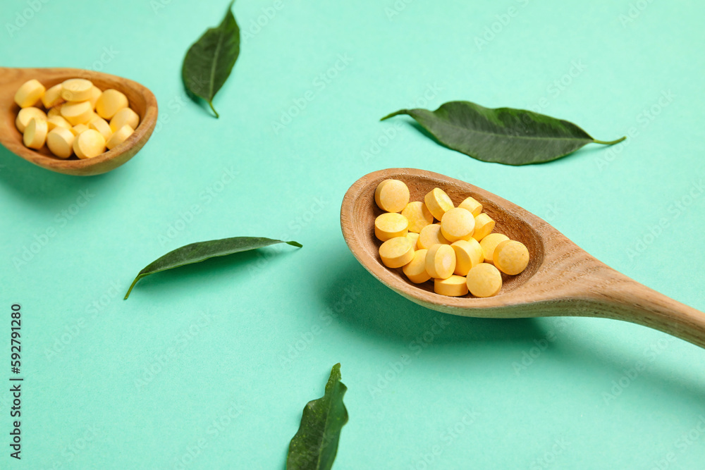 Spoons with pills and plant leaves on green background, closeup